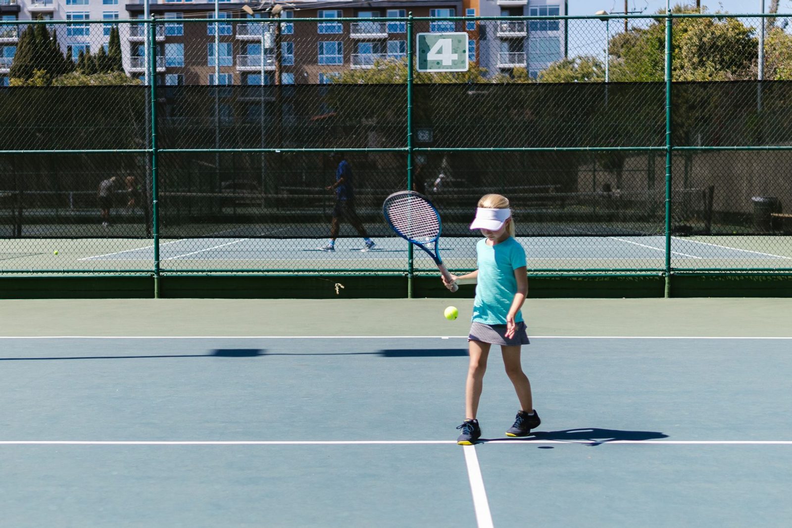 A young girl practising tennis on an outdoor court on a sunny day