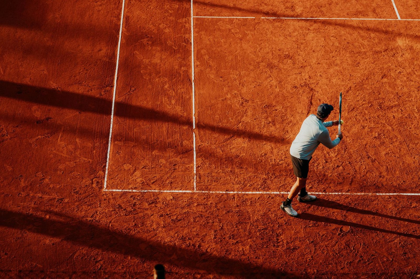 Overhead view of a player on a clay court casting a long shadow