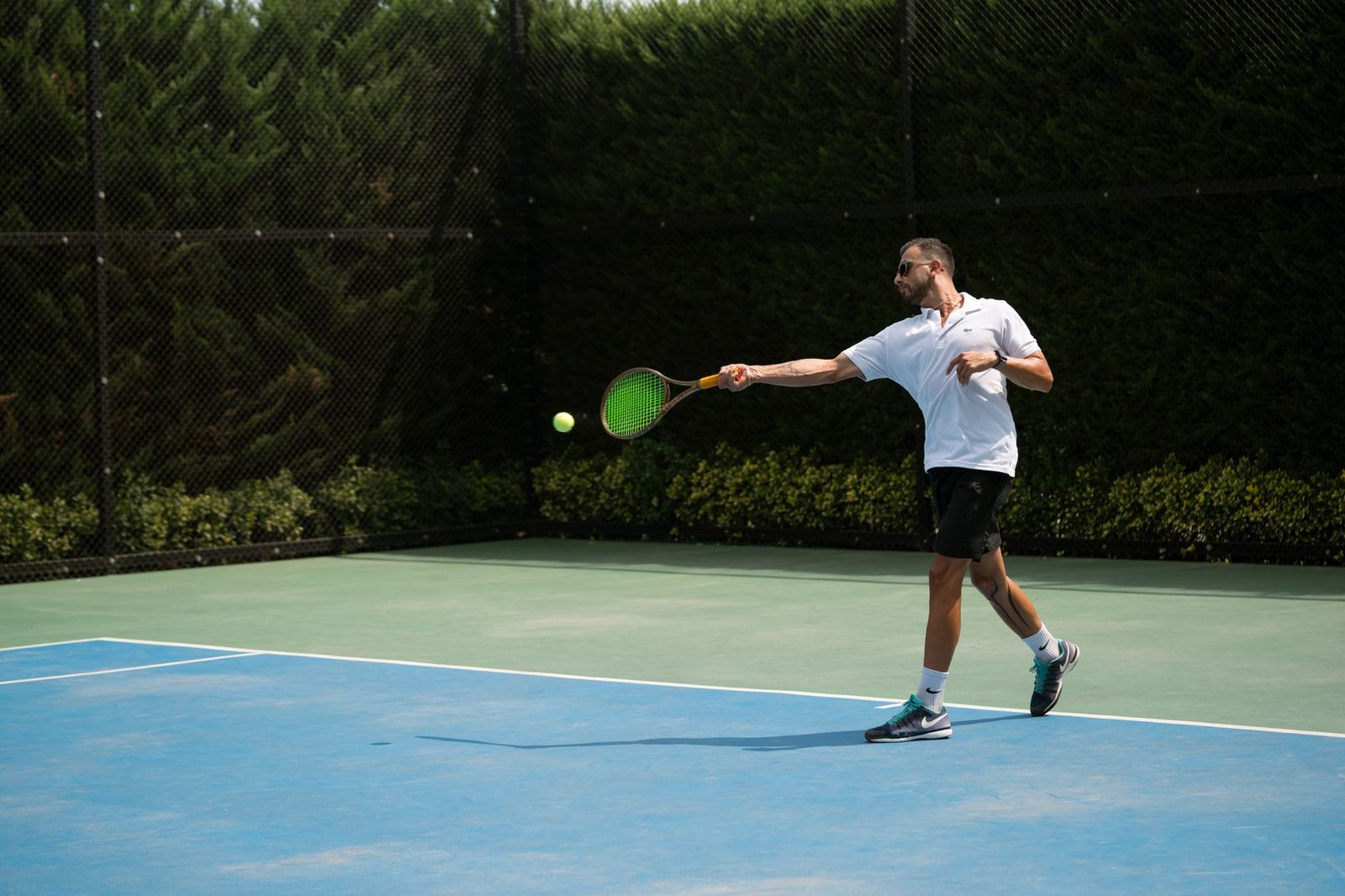 A man swinging his racquet on a sunny outdoor tennis court