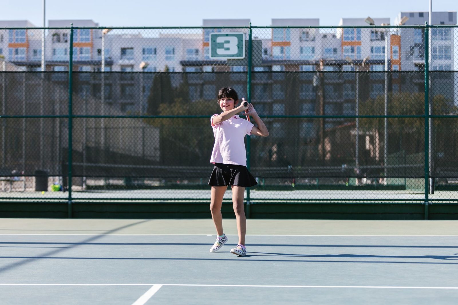 A young girl playing tennis on an outdoor court in bright daylight