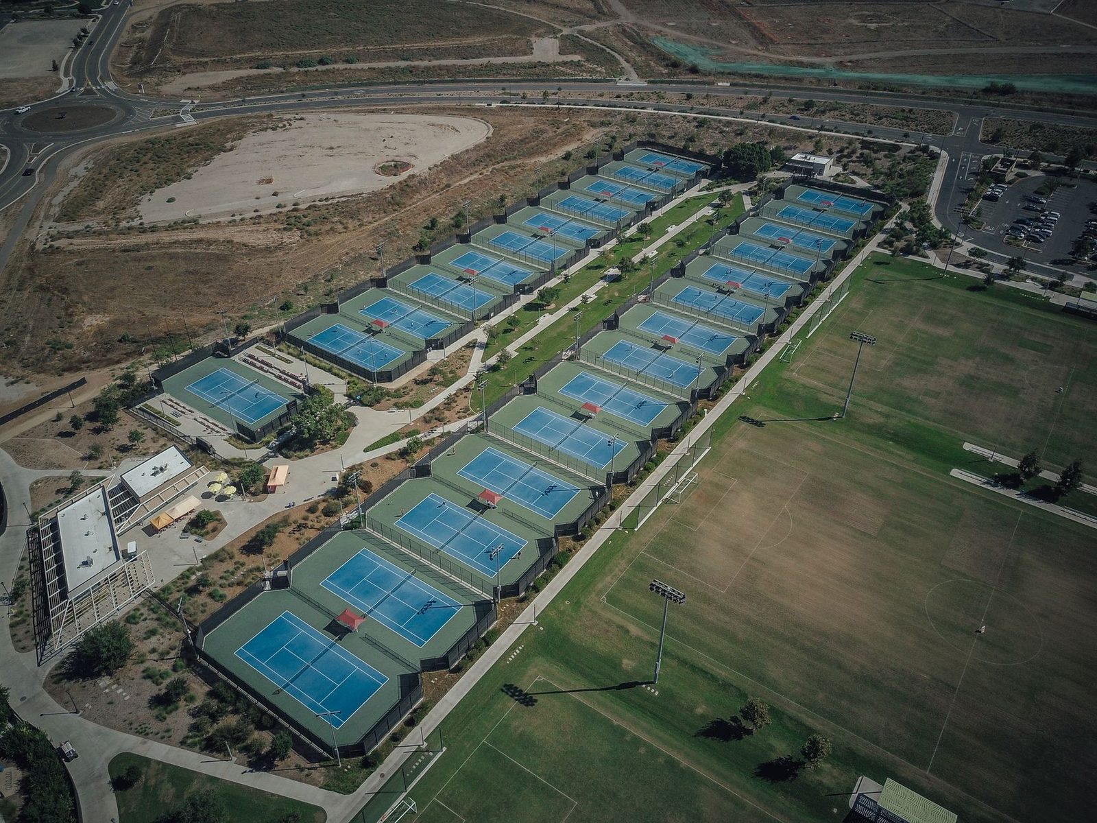 High-angle view of multiple tennis courts in a landscaped club setting