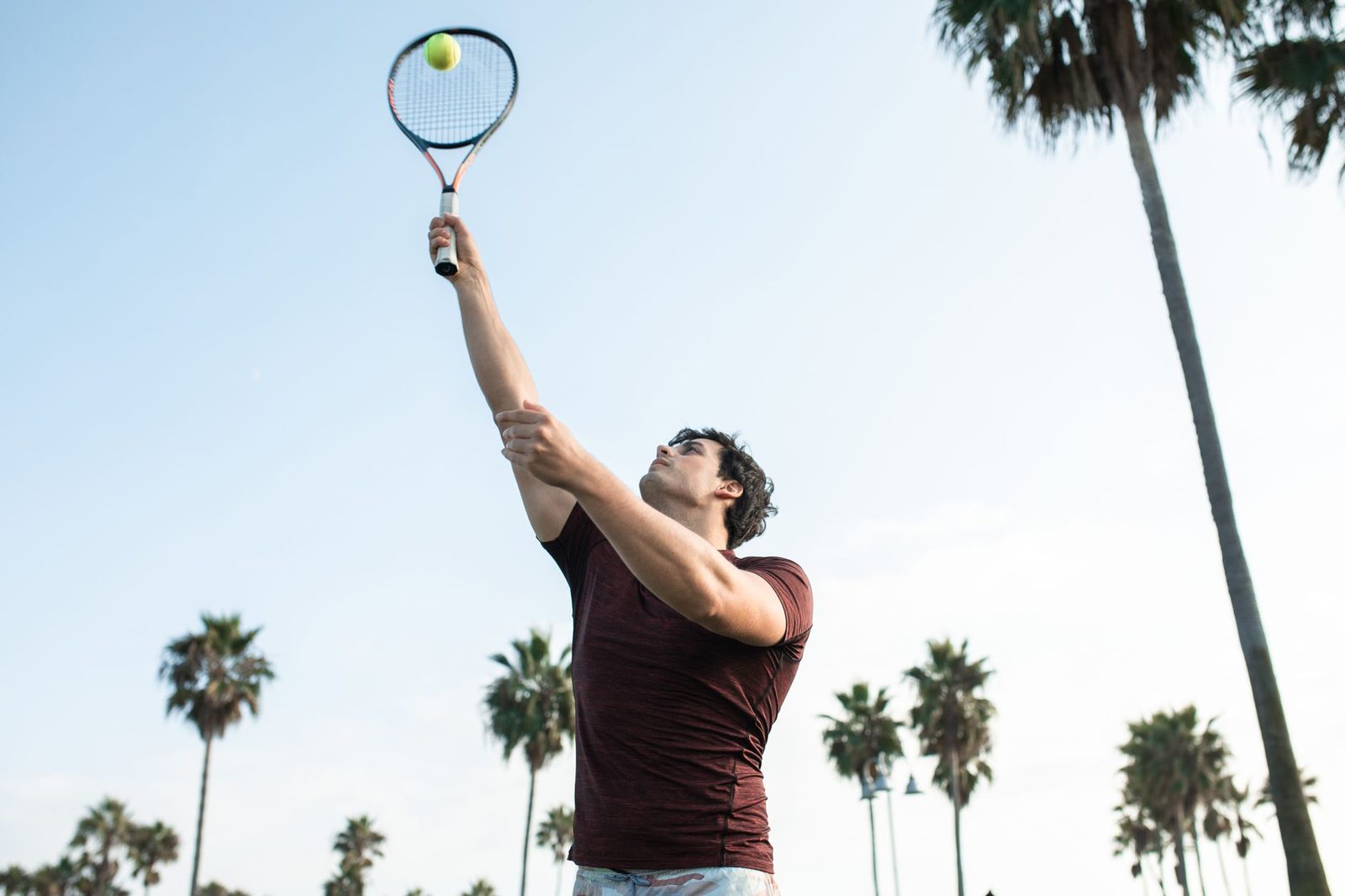 A young man playing tennis outdoors under a clear sky