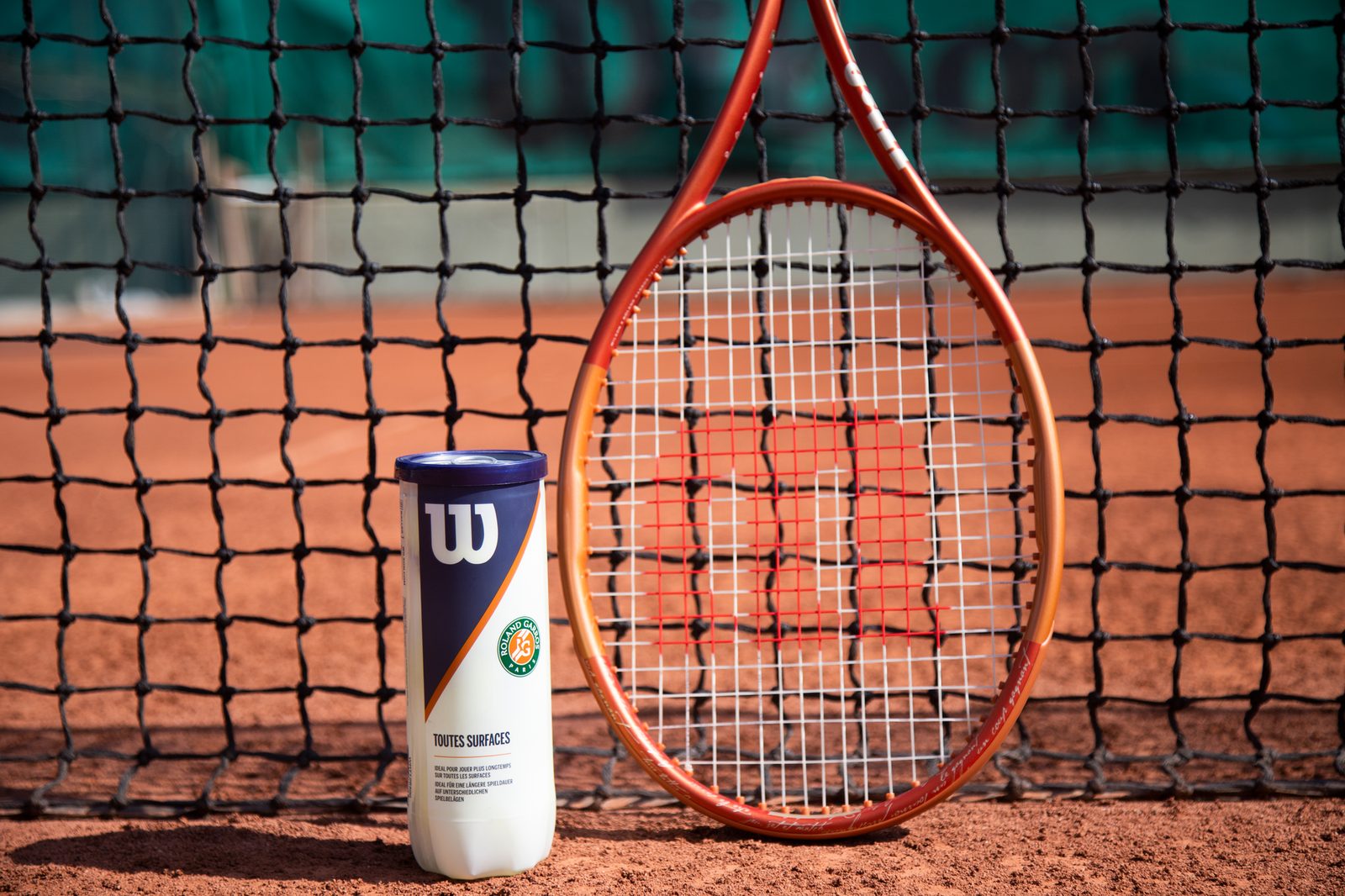 A tennis racquet and ball can in front of the net on a clay court