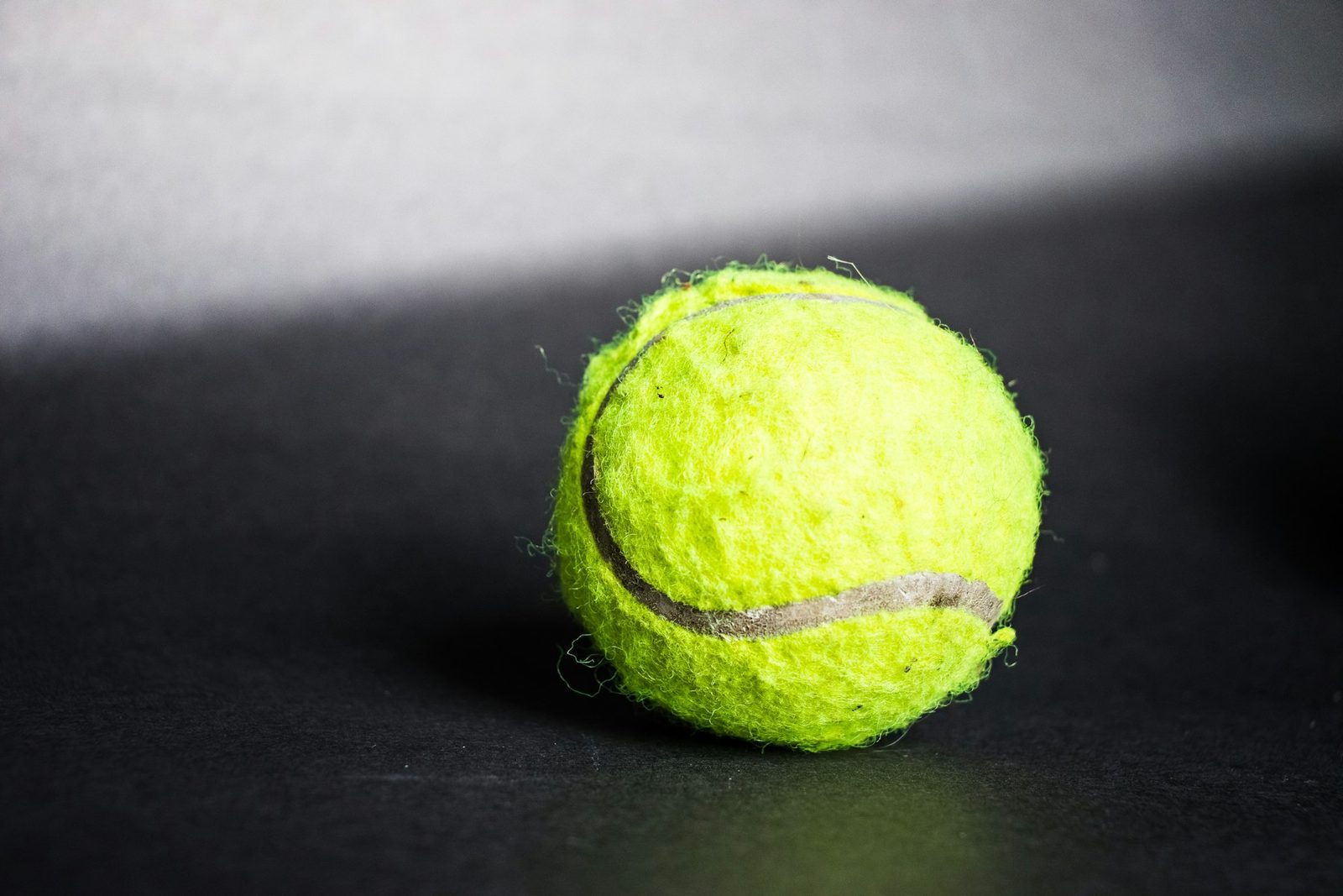 A green tennis ball on a dark surface