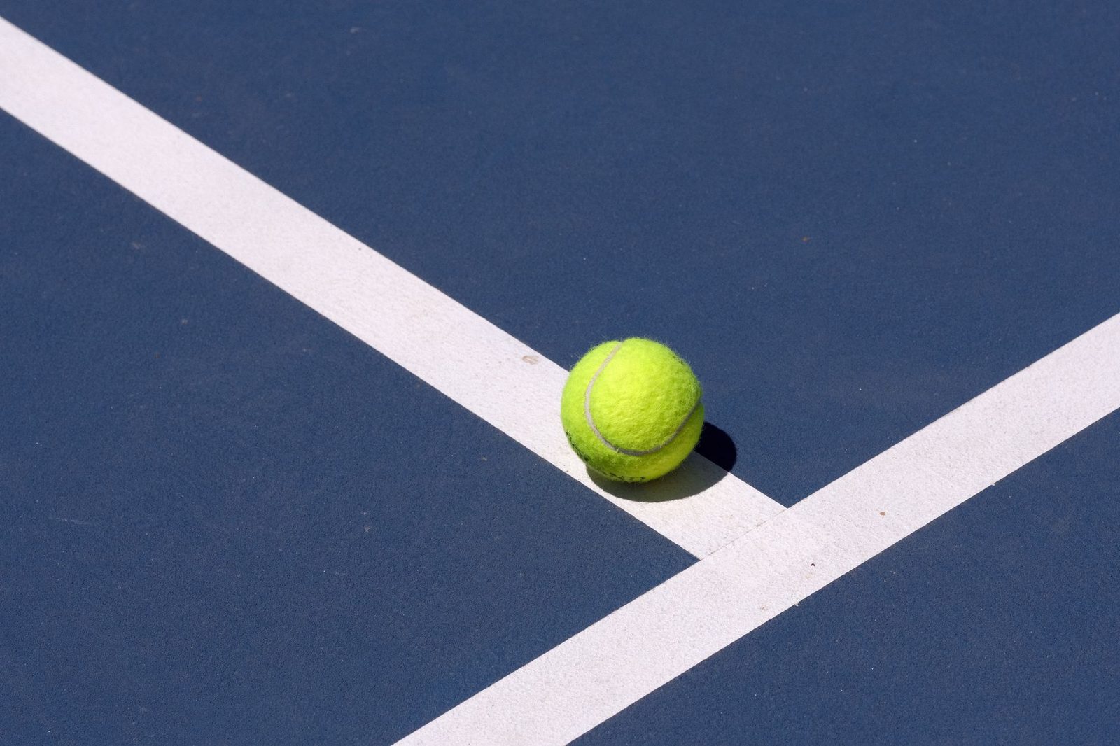 Close-up of a tennis ball beside the white line of a blue court