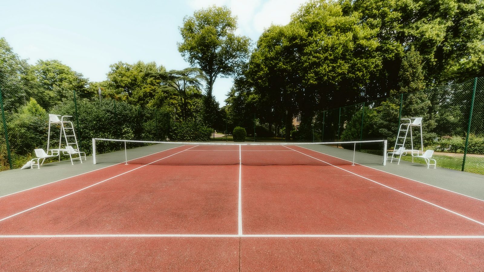 A tennis court seen from behind, with chairs and a racquet