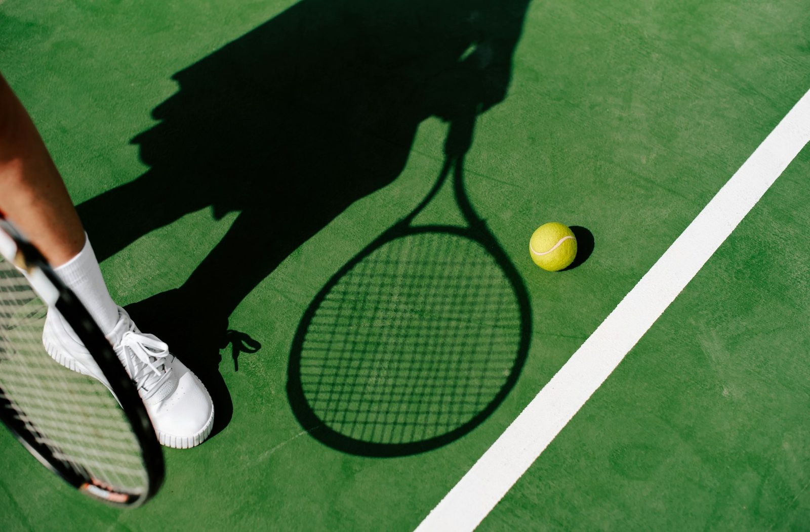 Shadow of a player holding a tennis racquet and ball on the court surface