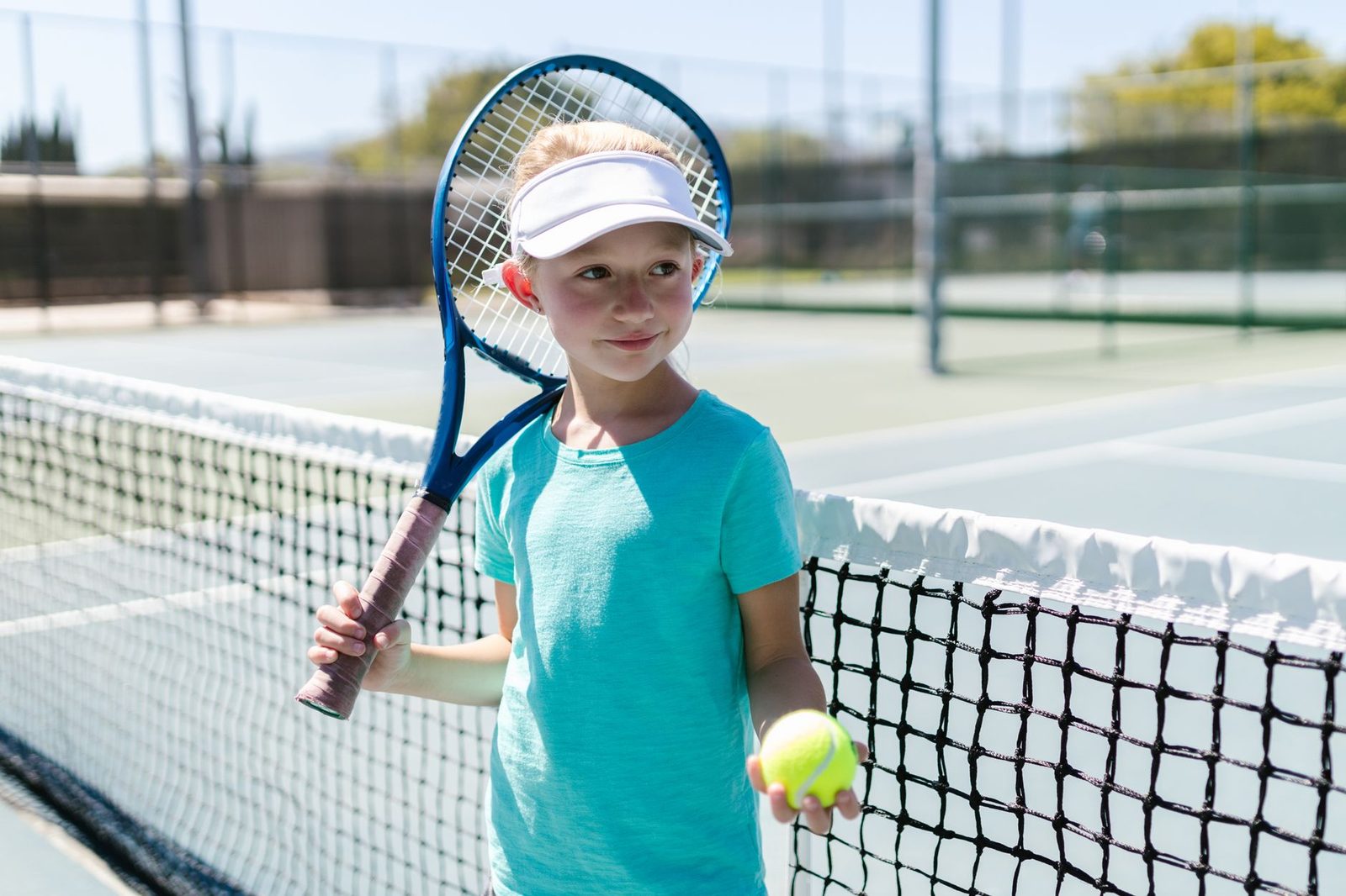 Smiling girl holding a tennis racquet and ball on an outdoor court