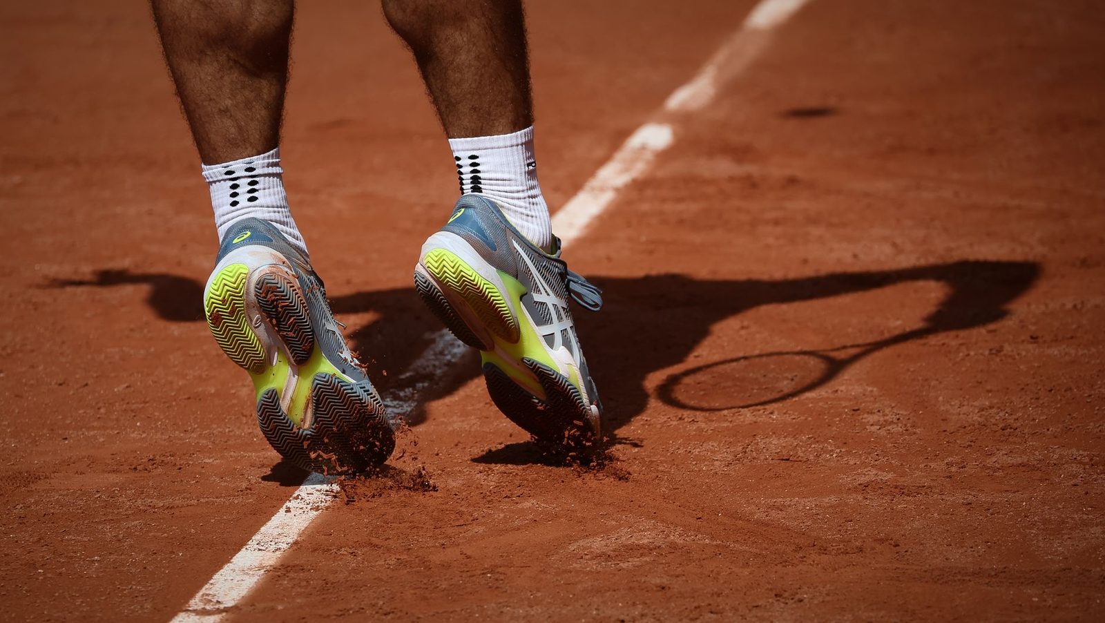 A tennis player moving on a clay court, showing their shoes