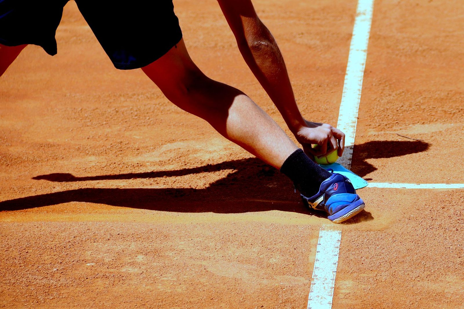 Player stretching wide to reach a ball on a sunny clay court