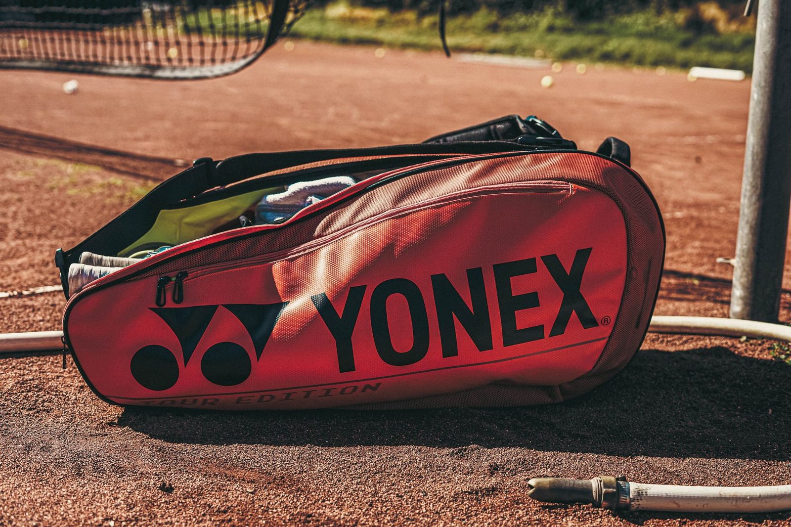 Close view of a tennis bag lying on a clay court in sunlight