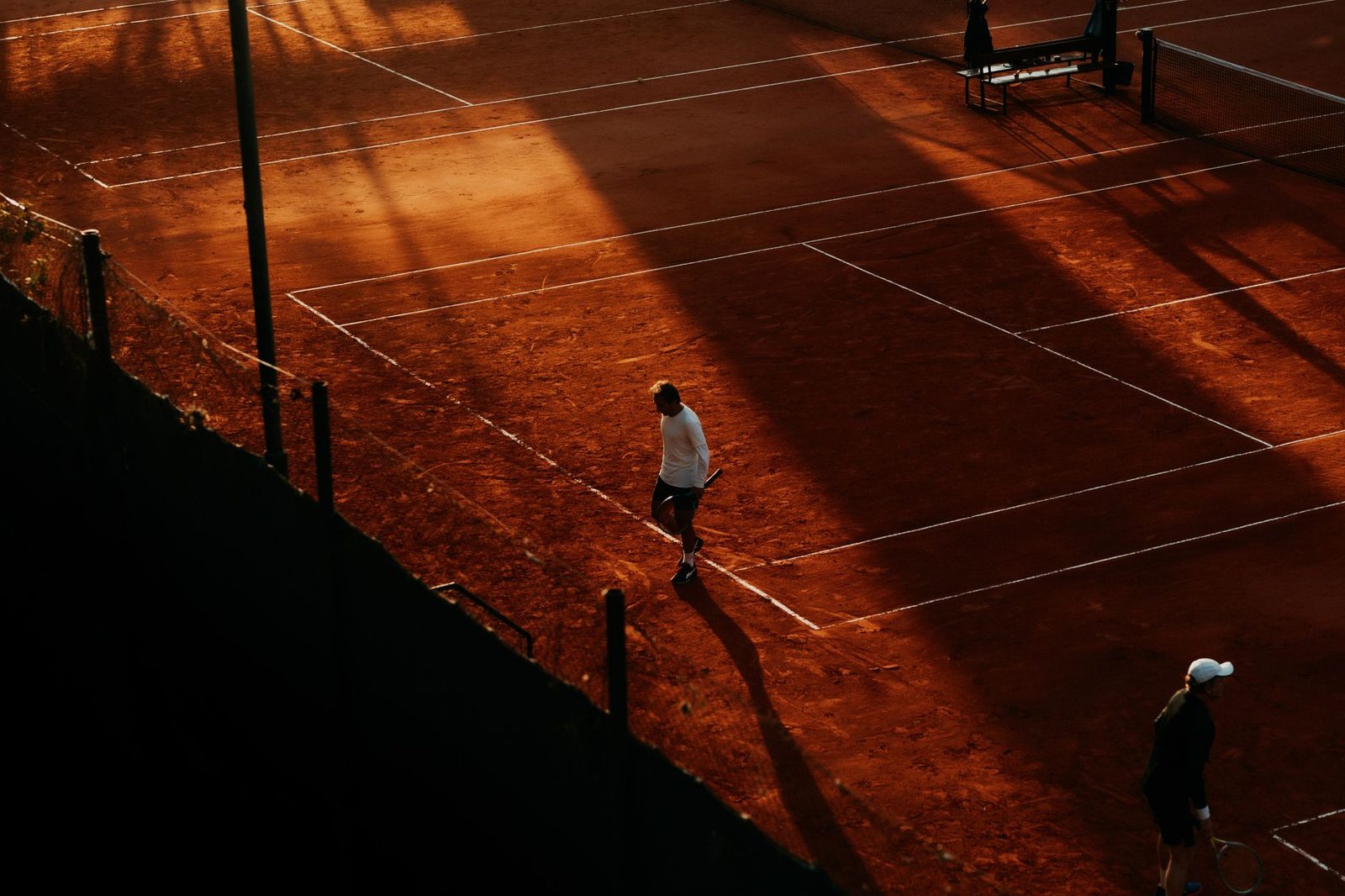Aerial view of a tennis match on a clay court at sunset