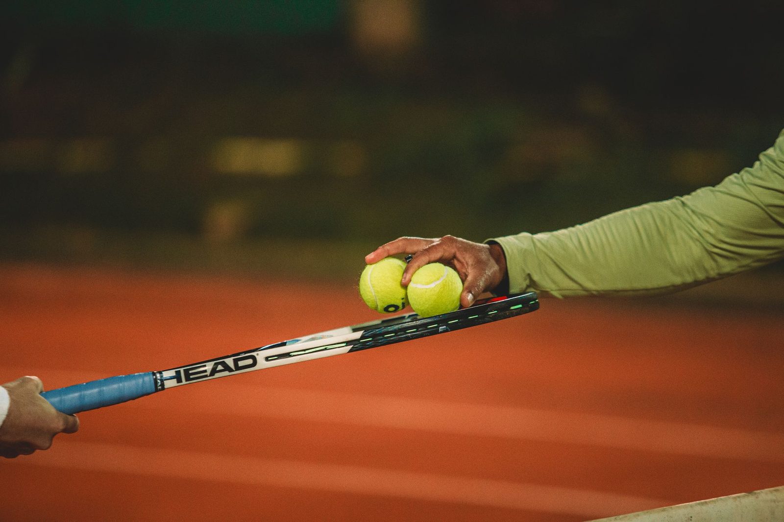 Two players exchanging tennis balls on a clay court at night