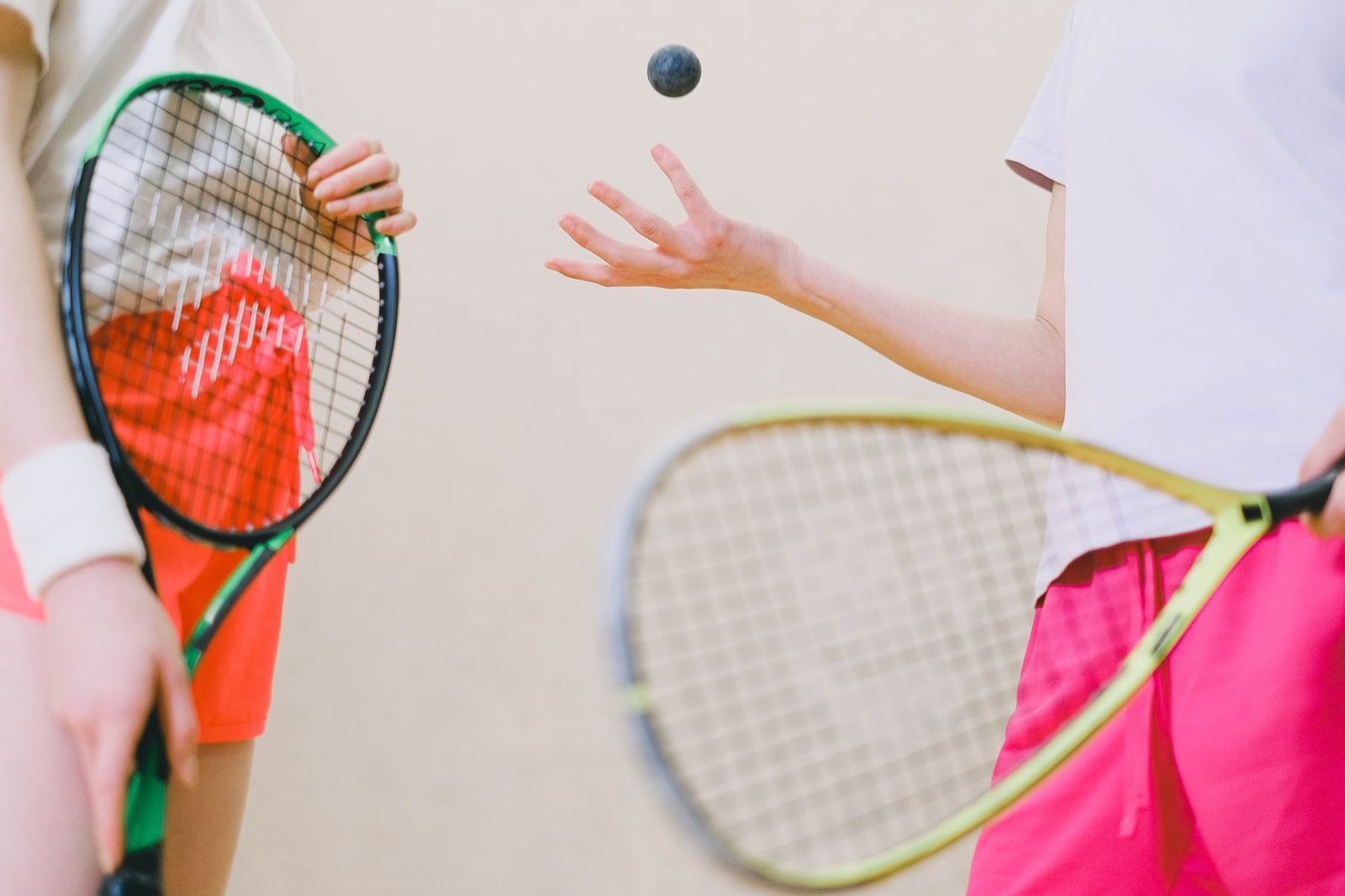 Two tennis players holding racquets and a ball indoors
