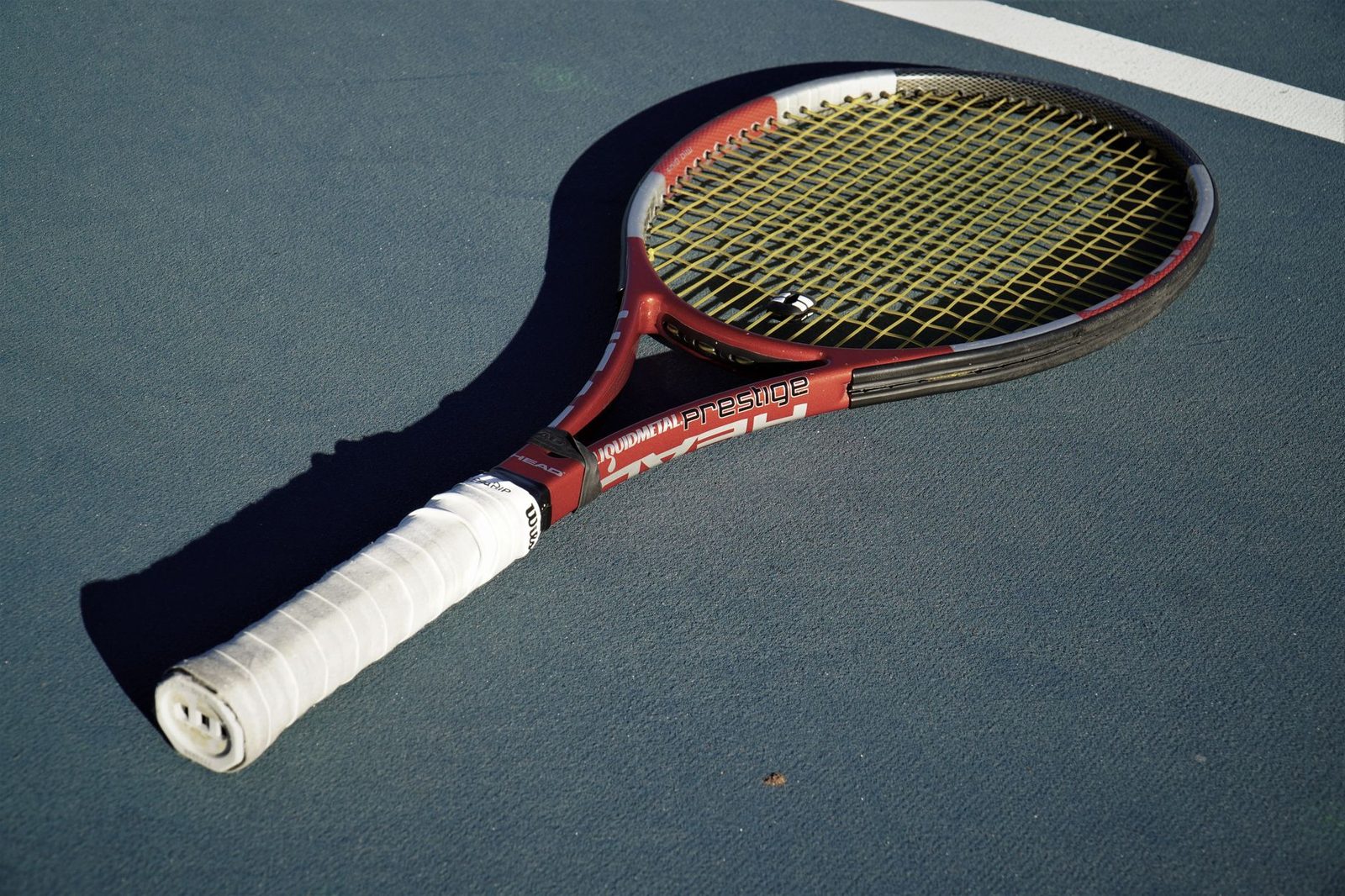 A tennis racquet resting on a blue court in sunlight
