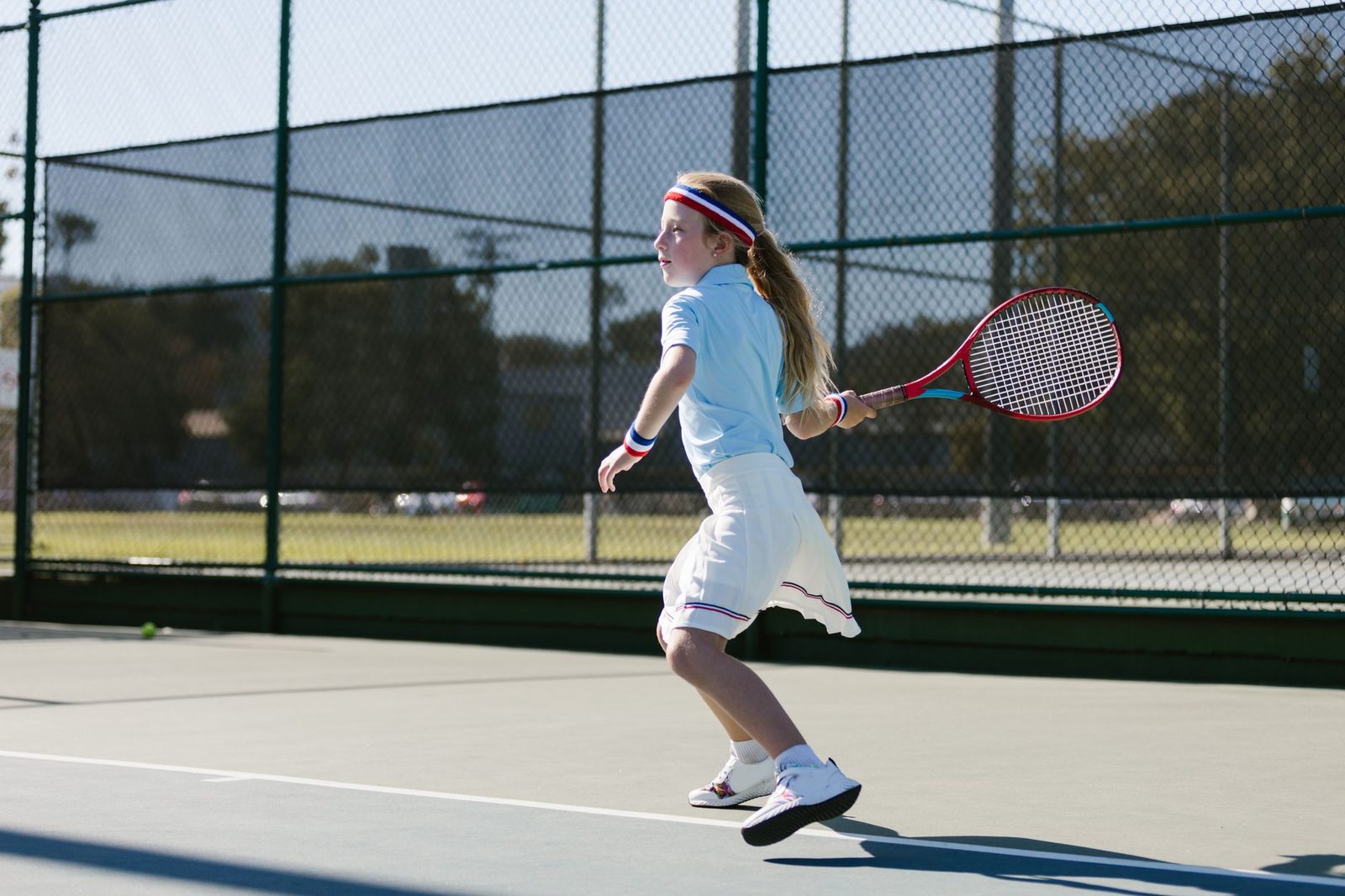 Young player hitting a forehand on an outdoor court on a sunny day