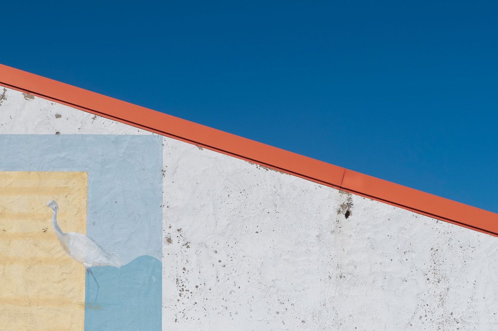 A plain white exterior wall against a clear blue sky
