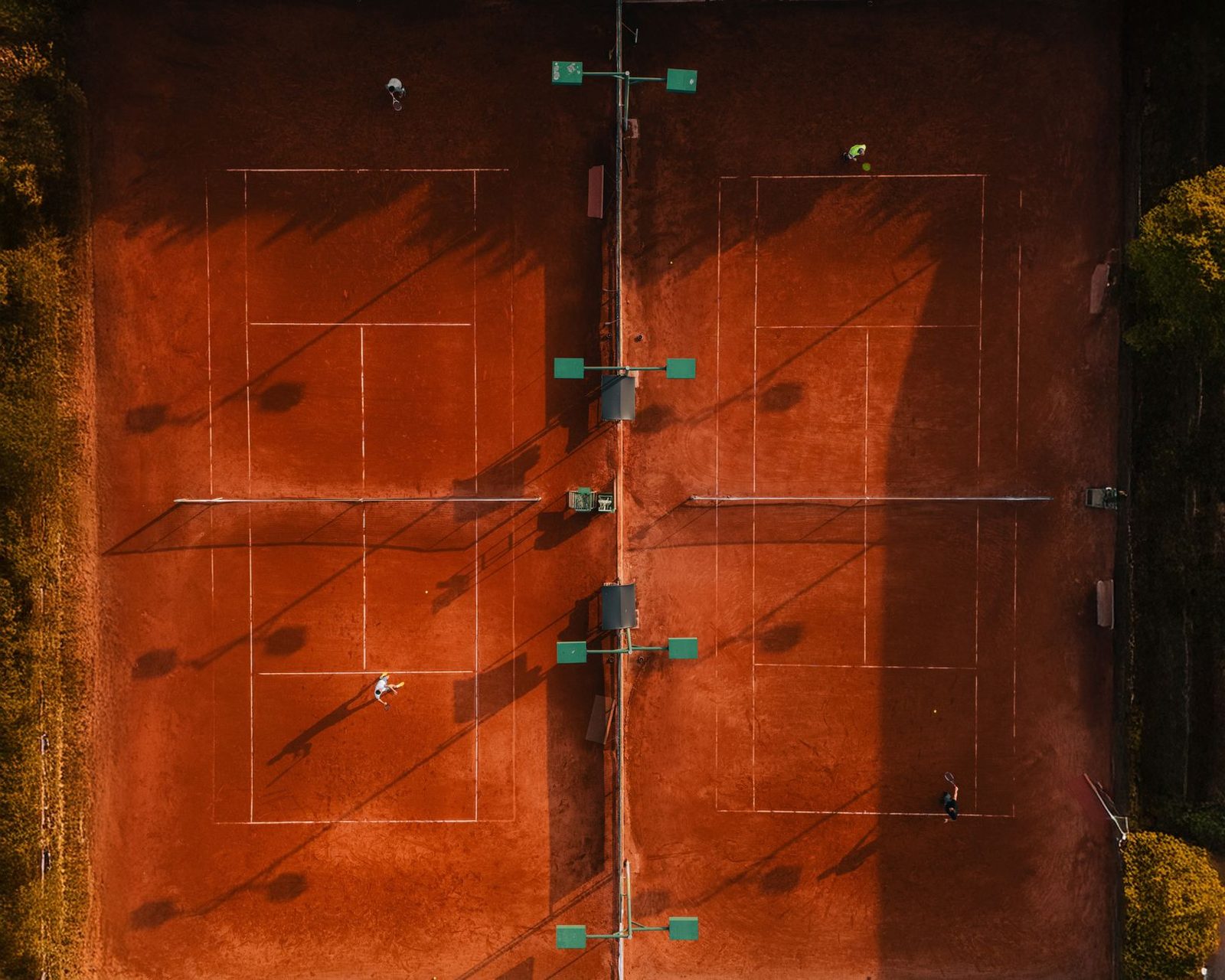 Aerial view of clay tennis courts with players at golden hour
