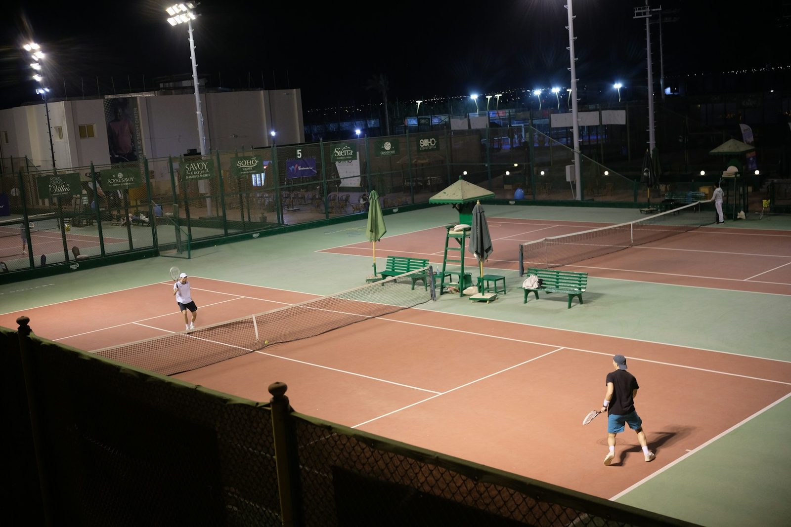 Two people playing tennis on an outdoor court at night