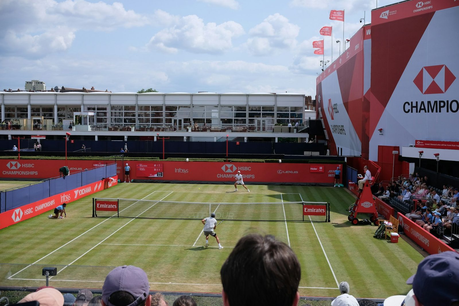 A tennis match being played on a grass court with spectators watching