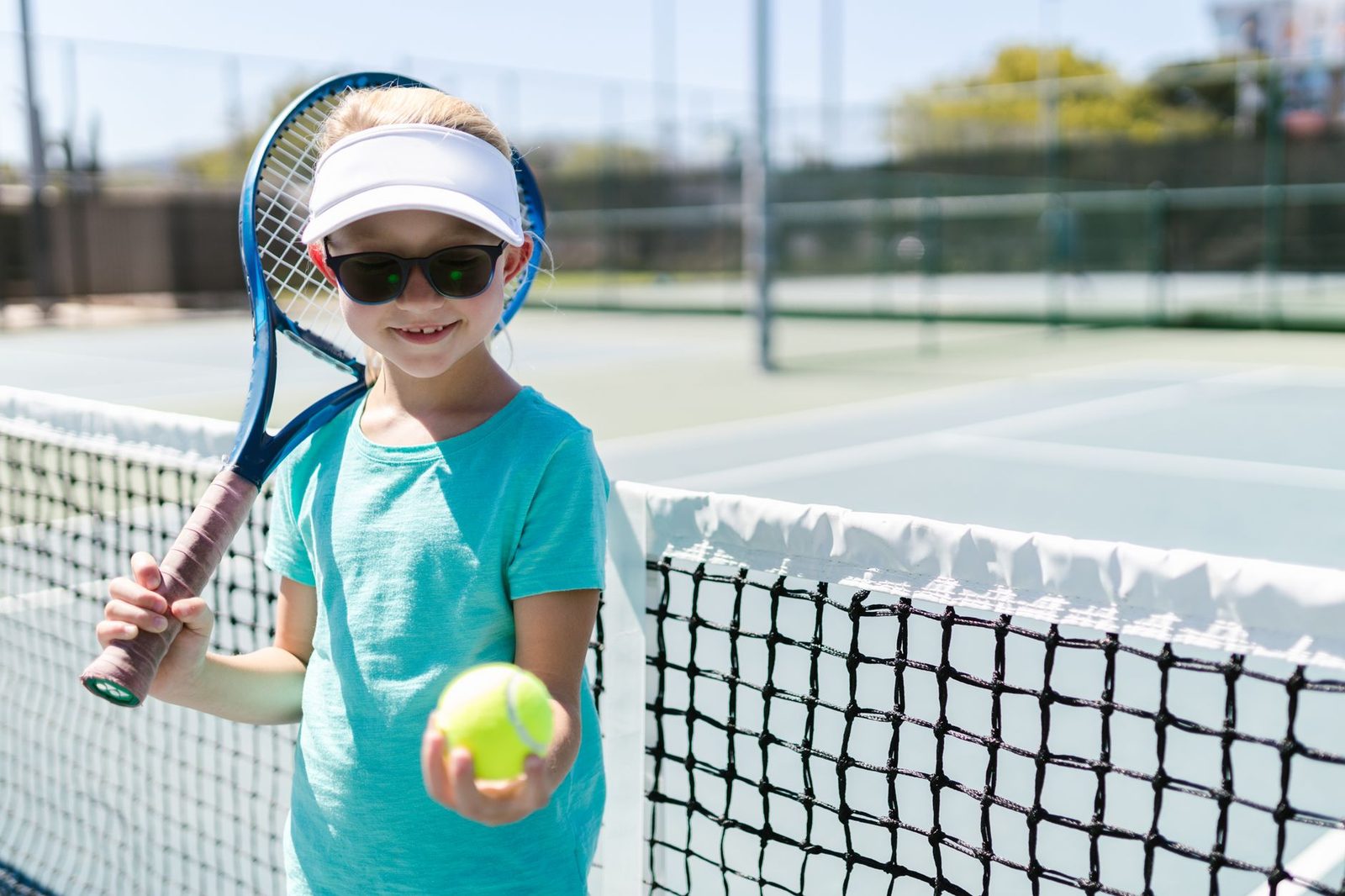 Smiling girl holding a tennis racquet and ball on a sunny court