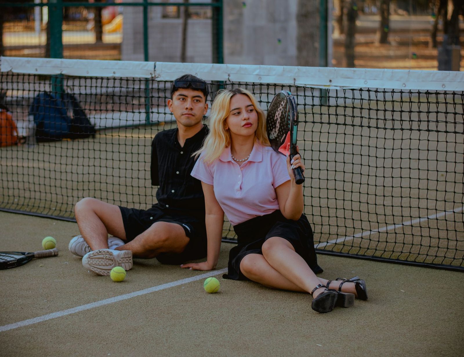 Two adult players sitting against the net with racquets and balls after a session