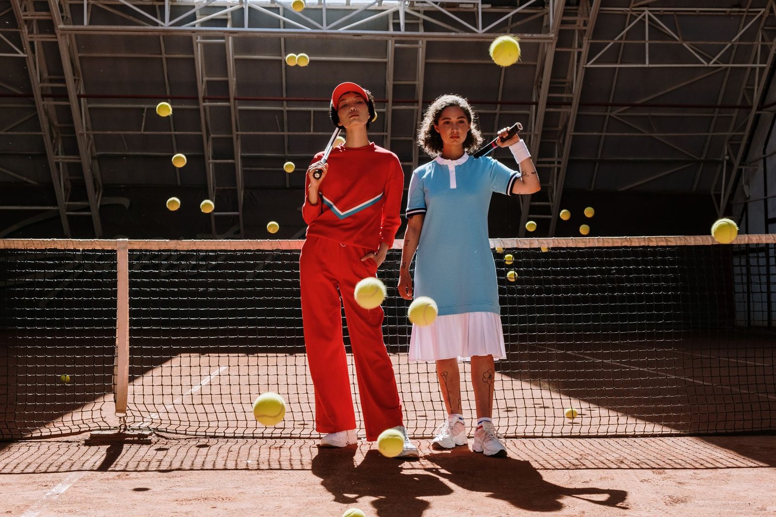 Two players with racquets on a court surrounded by bouncing tennis balls