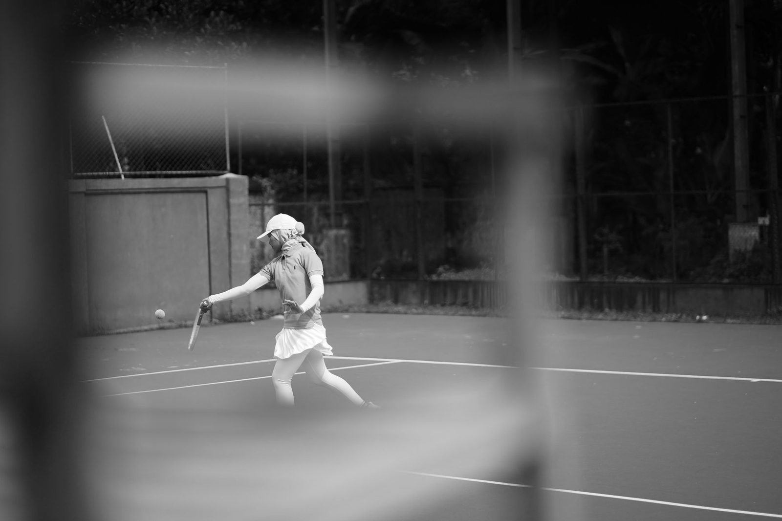 Black and white photograph of a tennis player mid-swing on an outdoor court