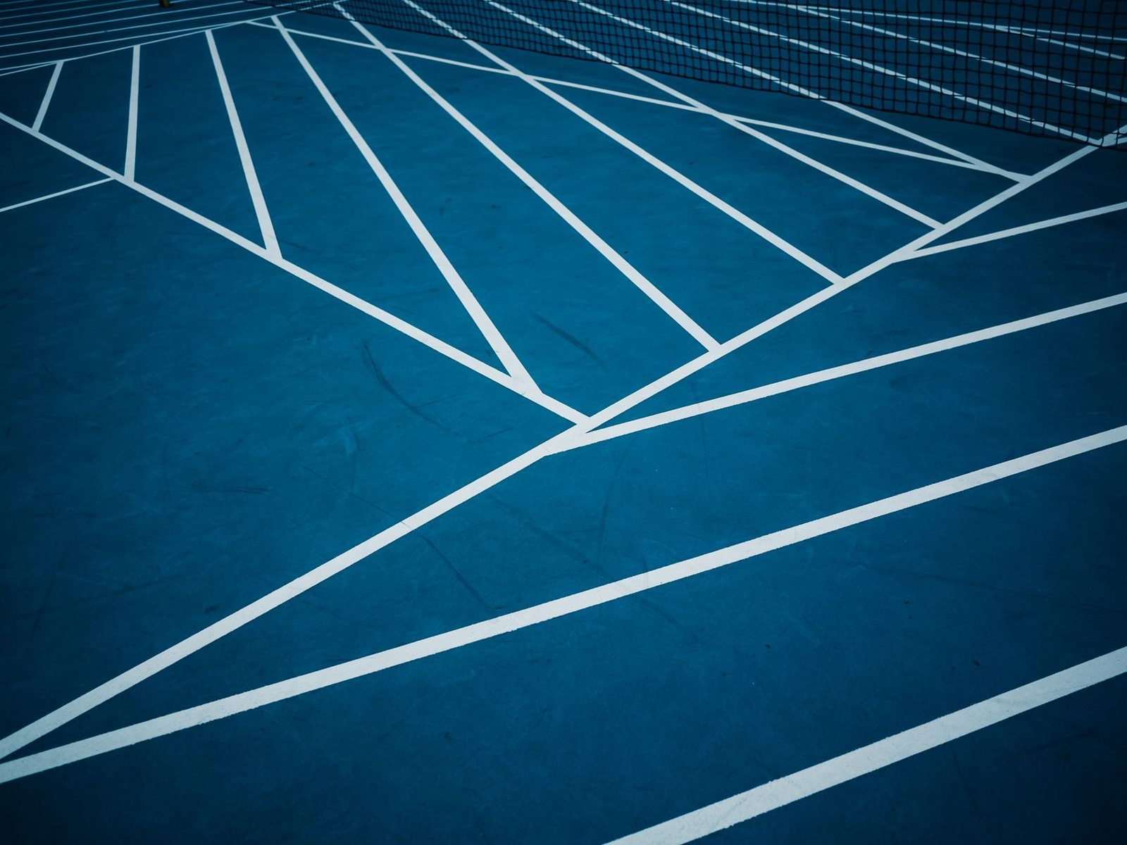 A blue hard tennis court with white line markings