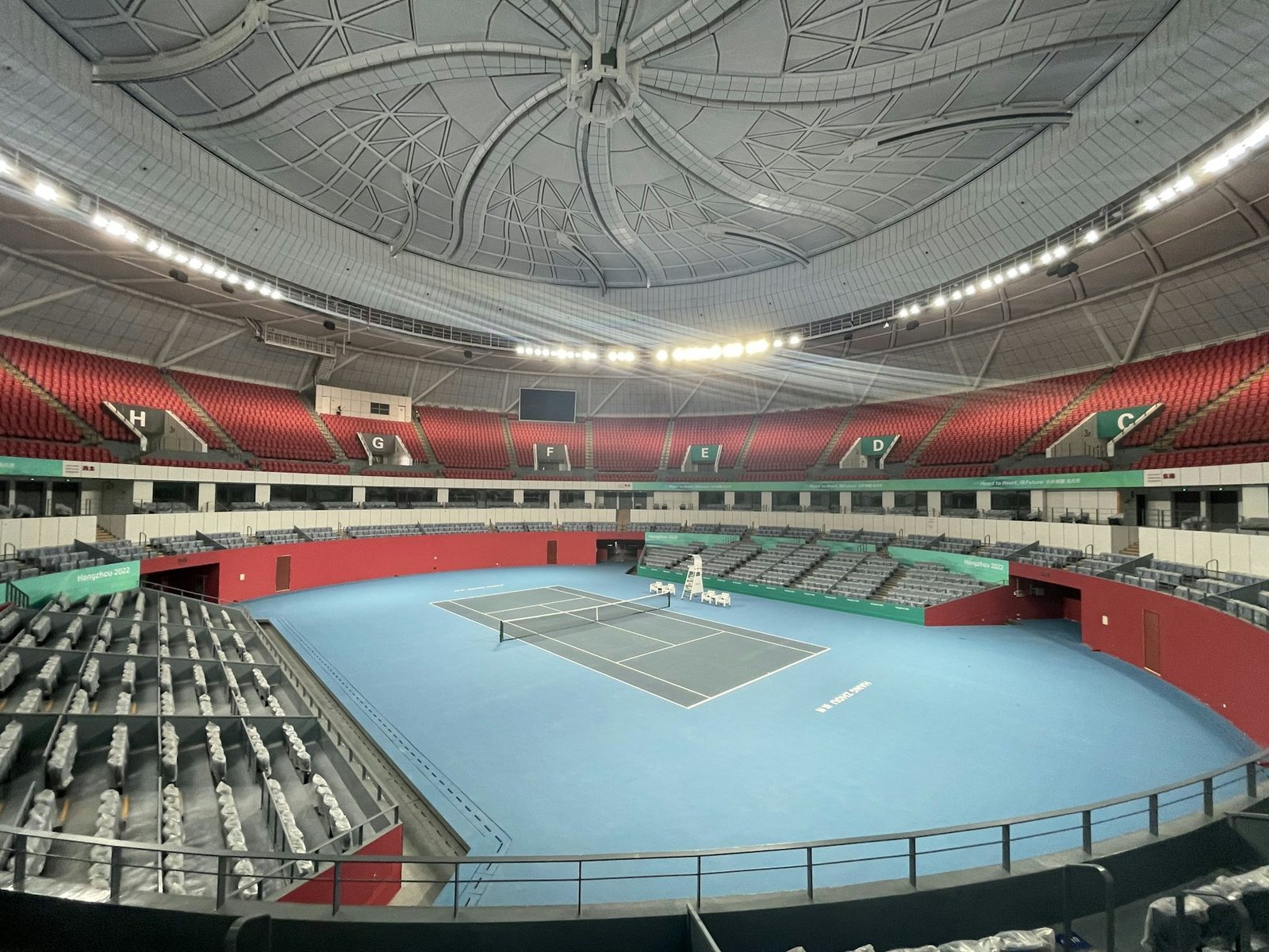 An indoor tennis court with a blue floor and seating