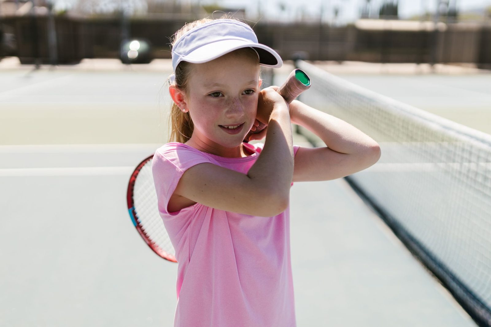 A cheerful young girl holding a tennis racquet on an outdoor court