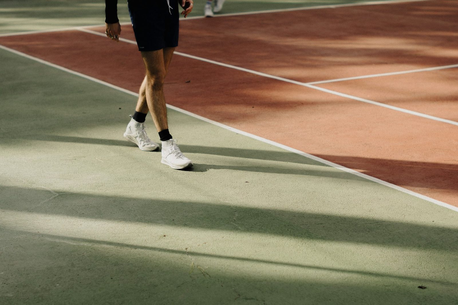 Teenage tennis player walking across an outdoor court