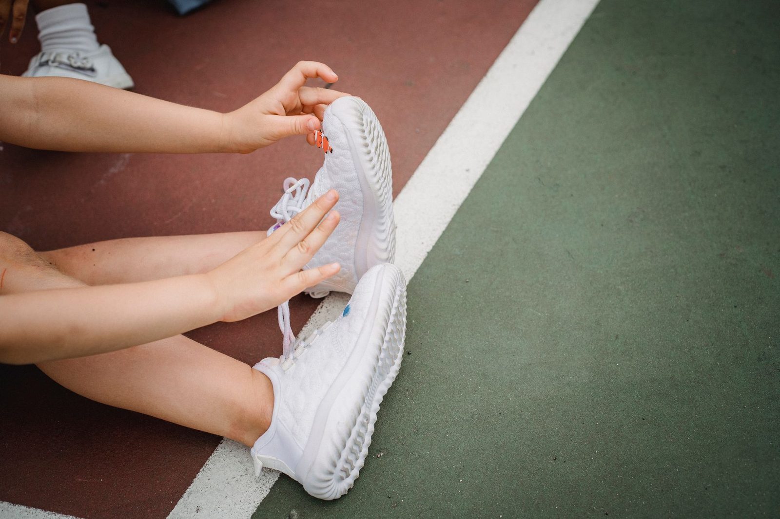 A child adjusting white trainers while sitting on a sports court
