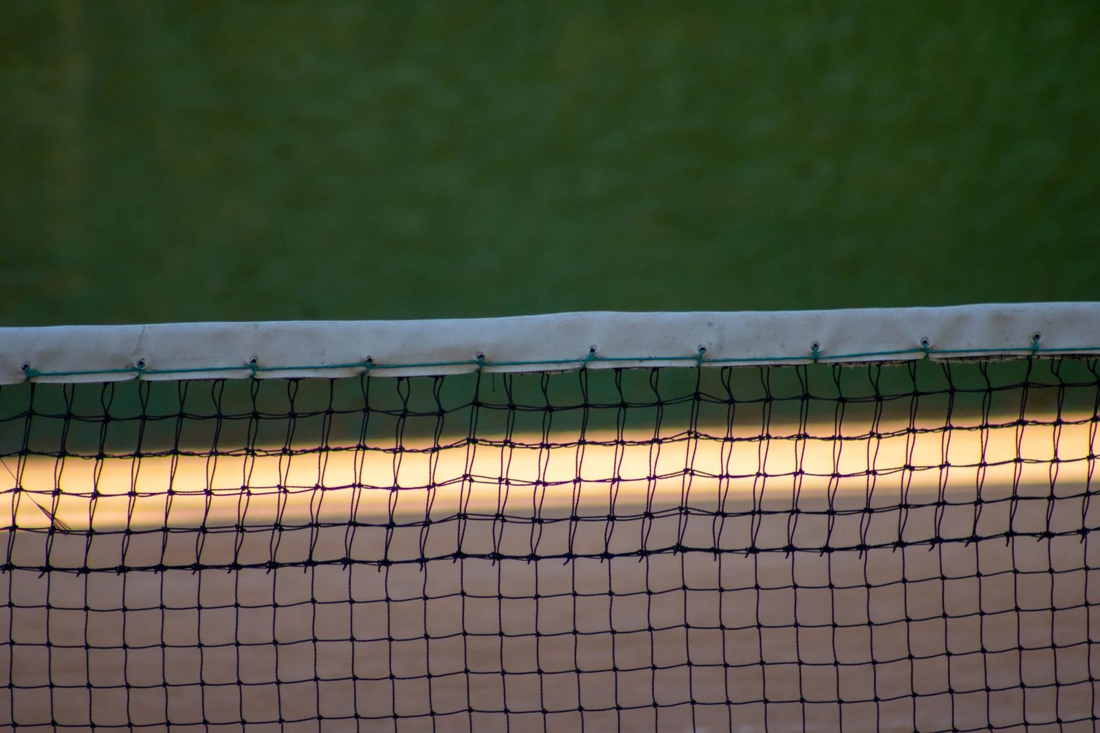 Detailed view of a tennis court net at dusk against a green court