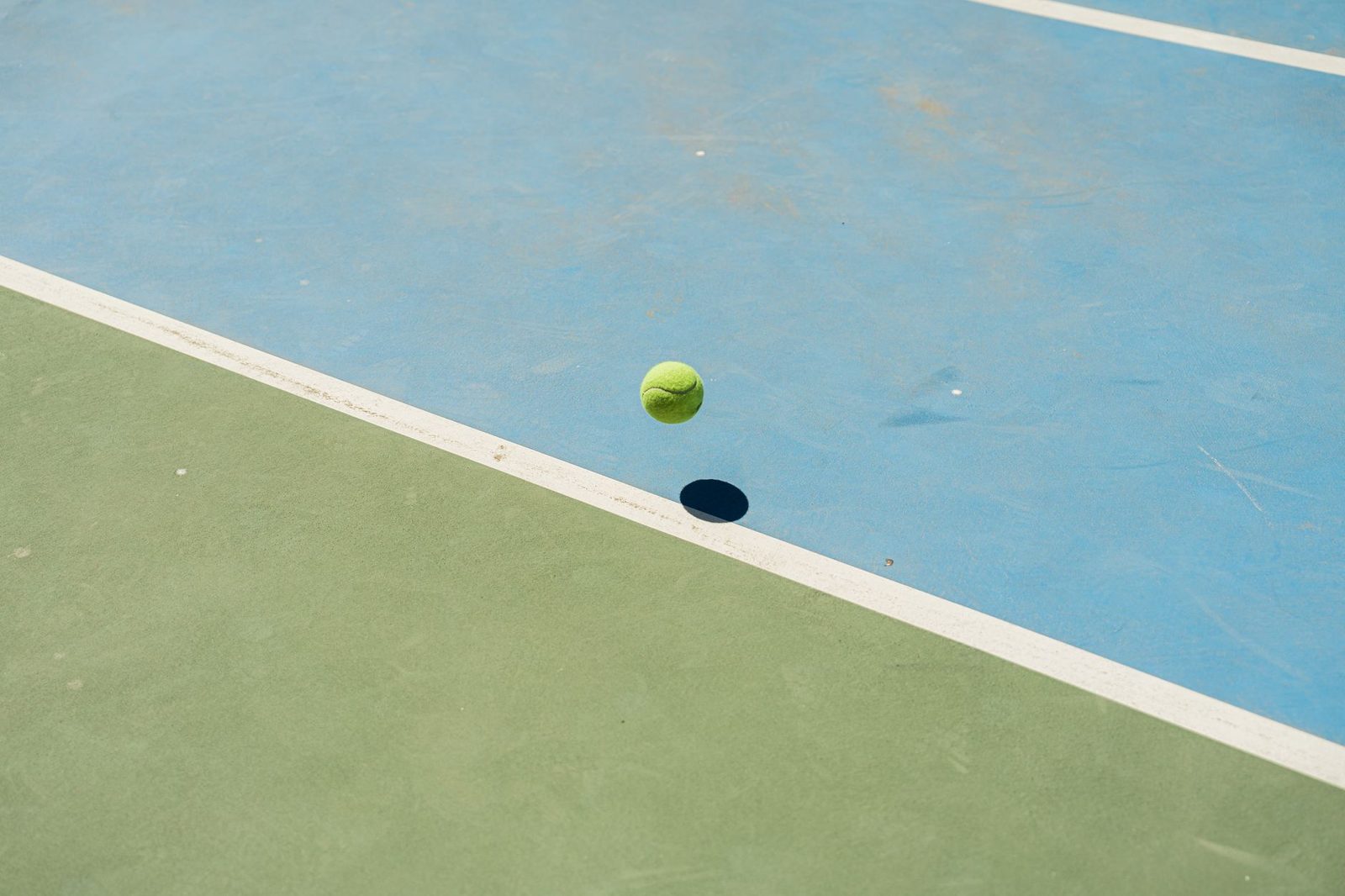 A tennis ball bouncing in mid-air, casting a shadow on the court