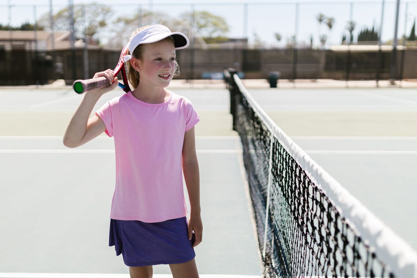 A cheerful young girl on a tennis court holding a racquet
