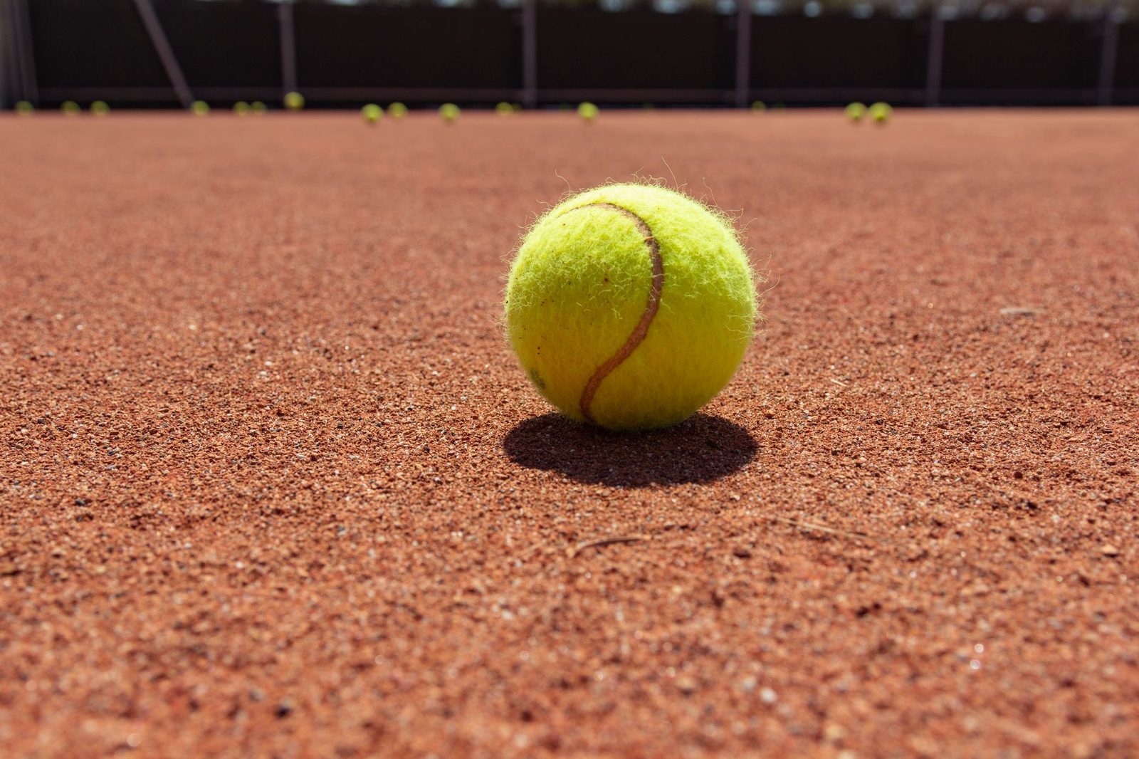 Yellow tennis ball resting on a clay court surface