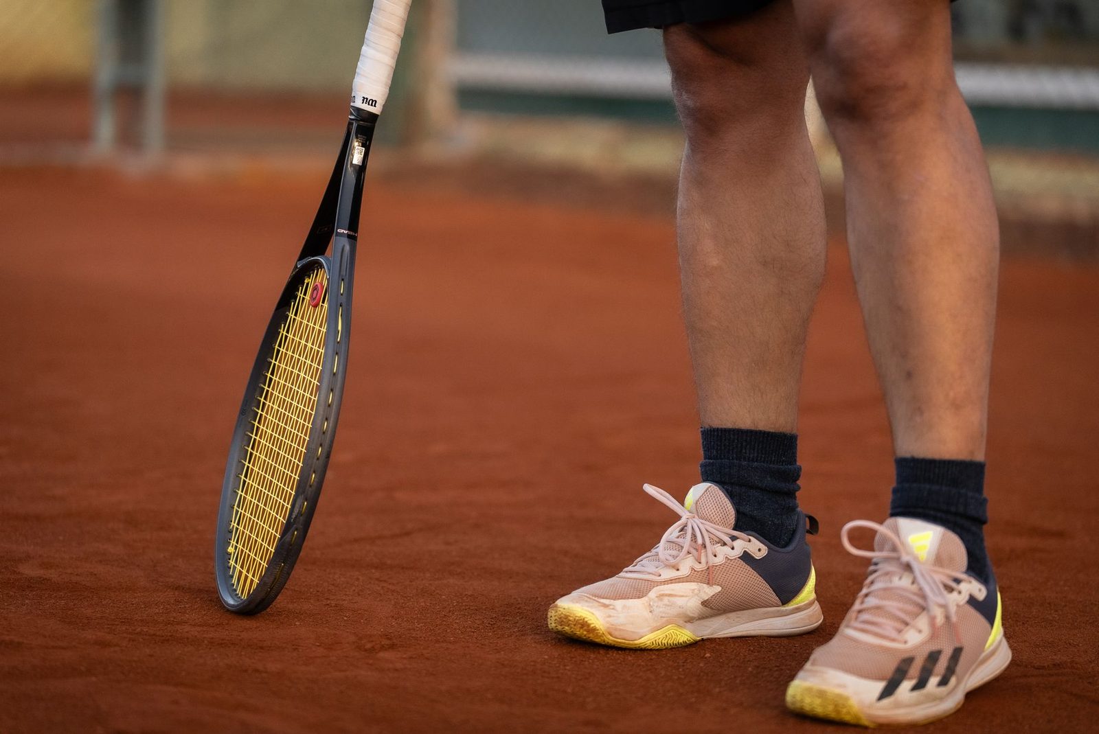 Close view of a racquet and a player's shoes on a clay court