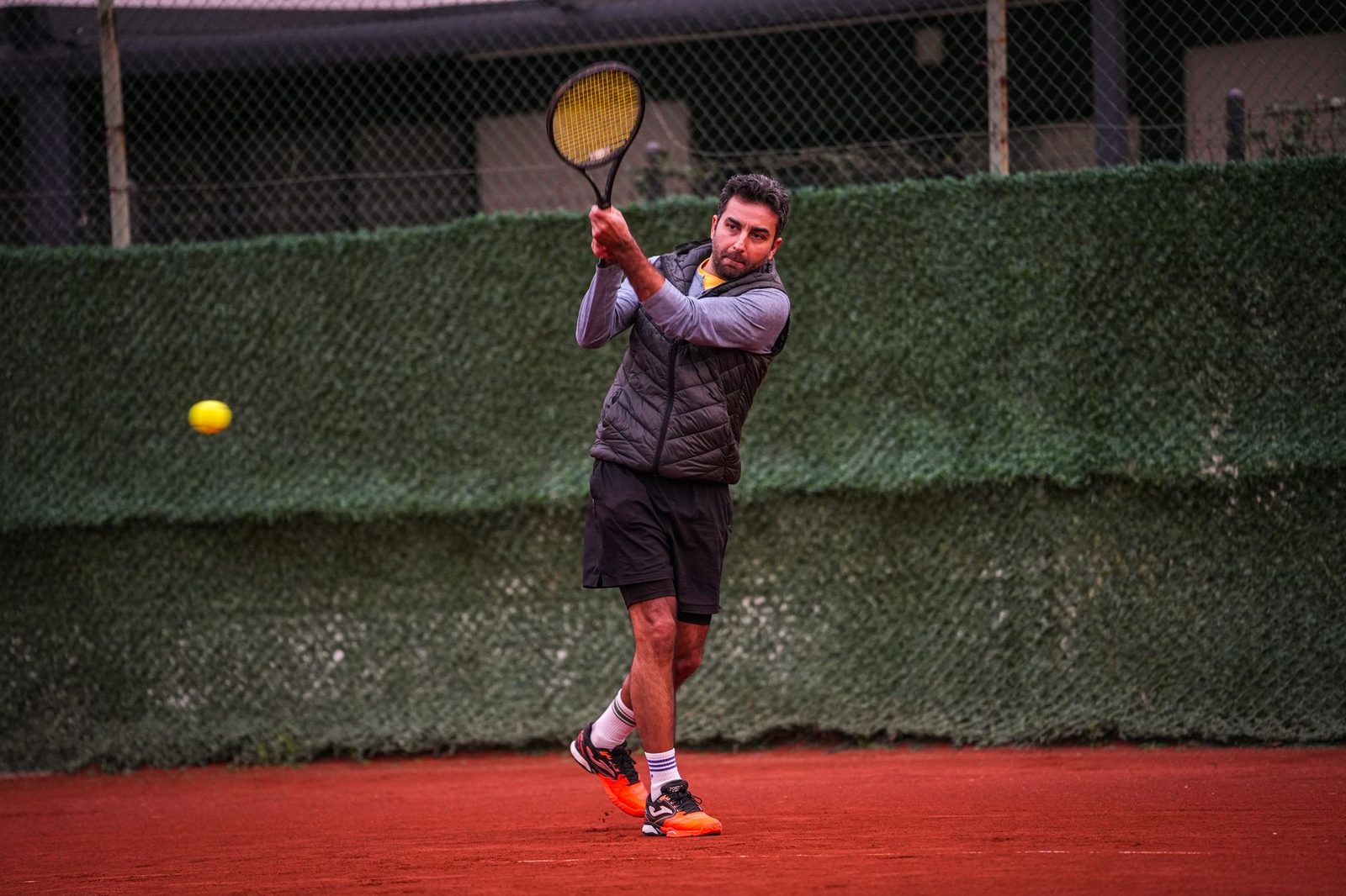 A focused player practising on a clay tennis court