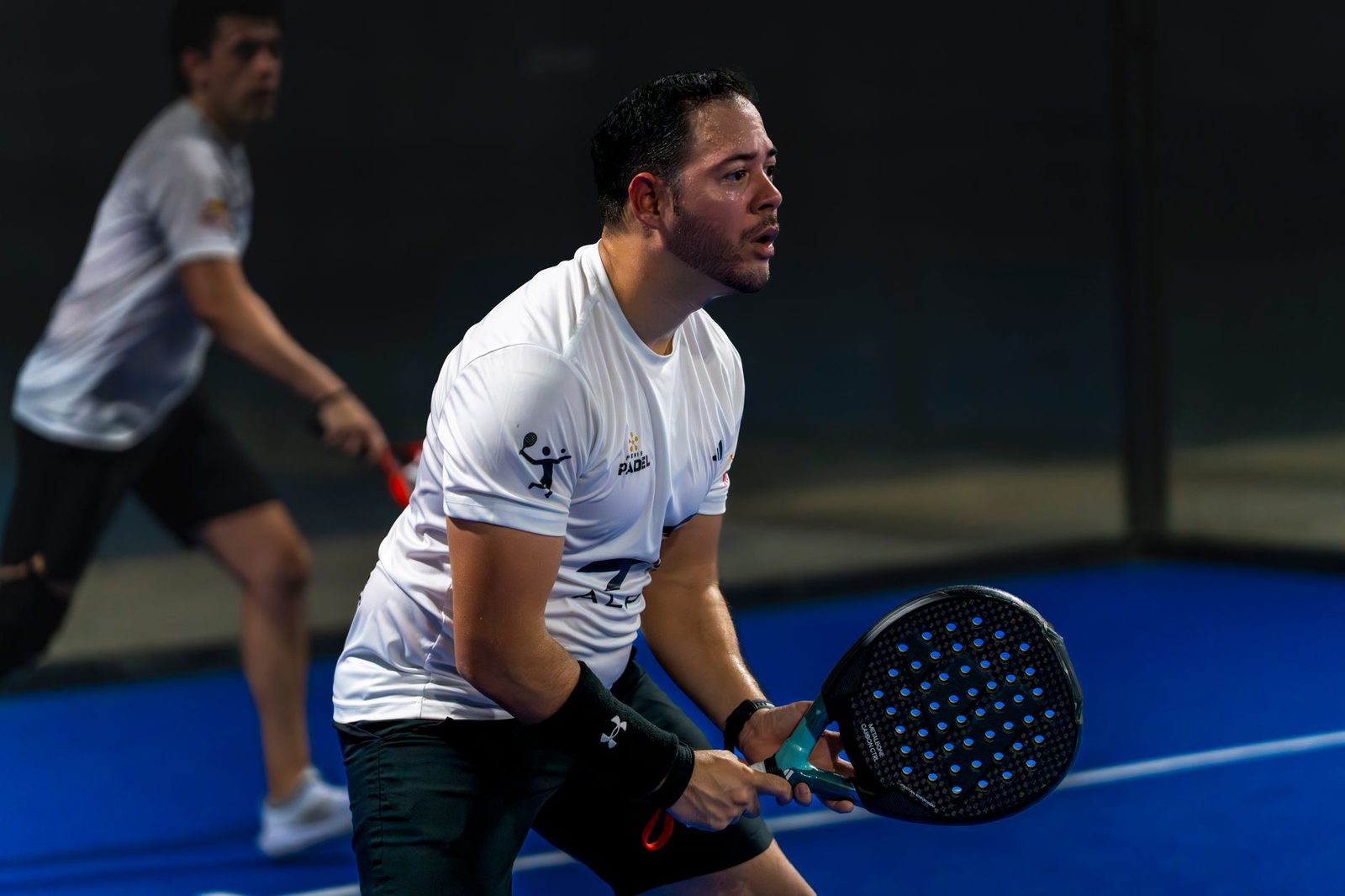 Two men playing a padel match on a bright blue indoor court