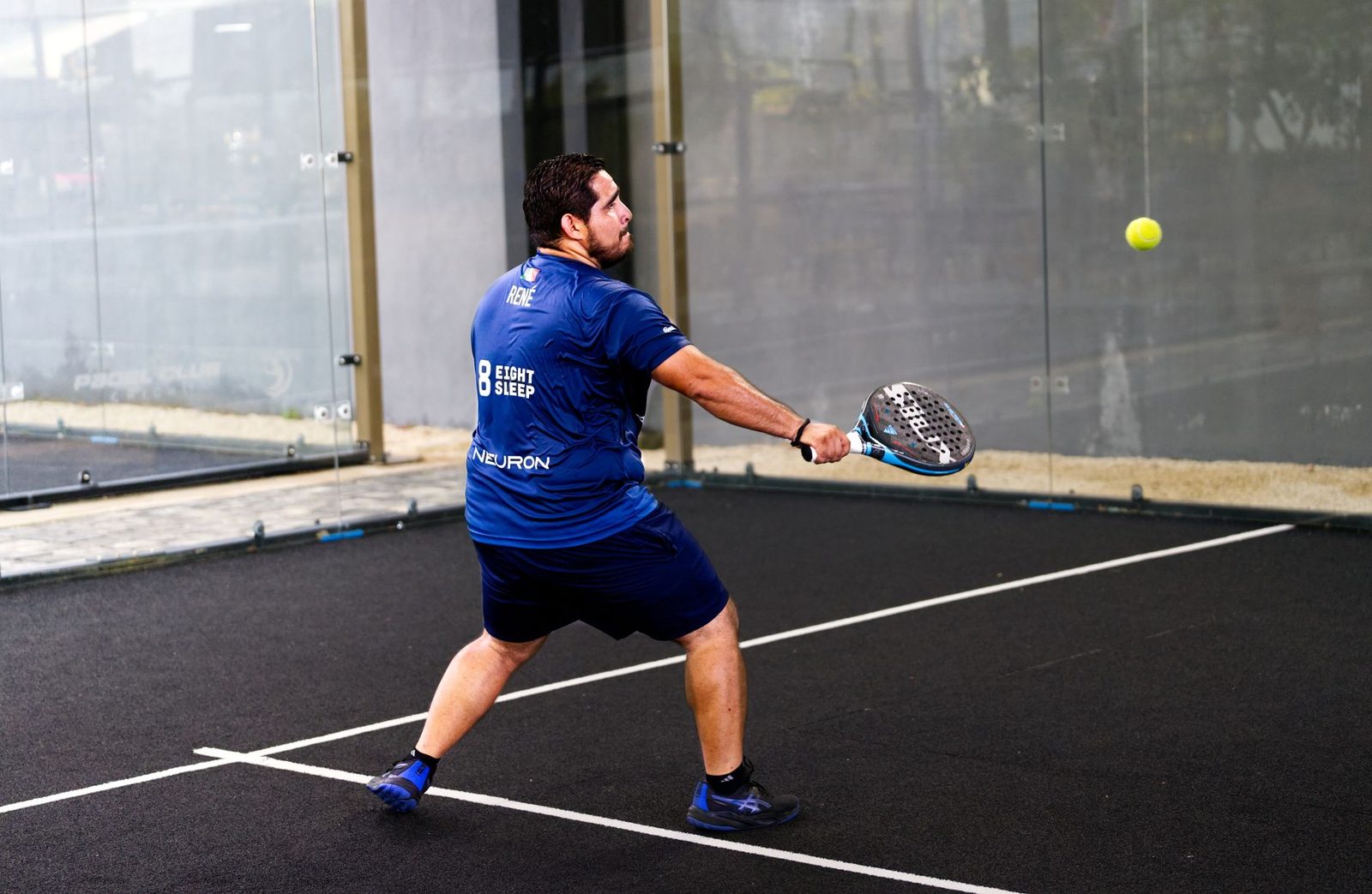Padel player striking the ball low on an indoor court