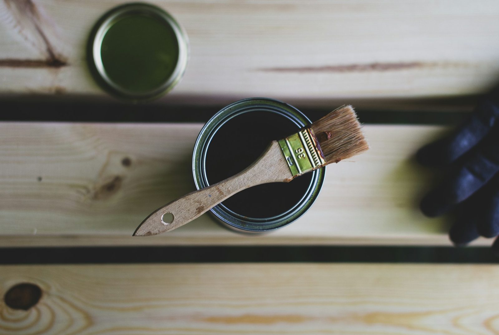A paint can with a brush resting on top, ready for sealing timber
