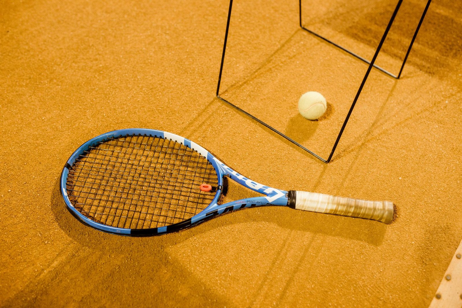 Blue tennis racquet and ball resting on an indoor clay court