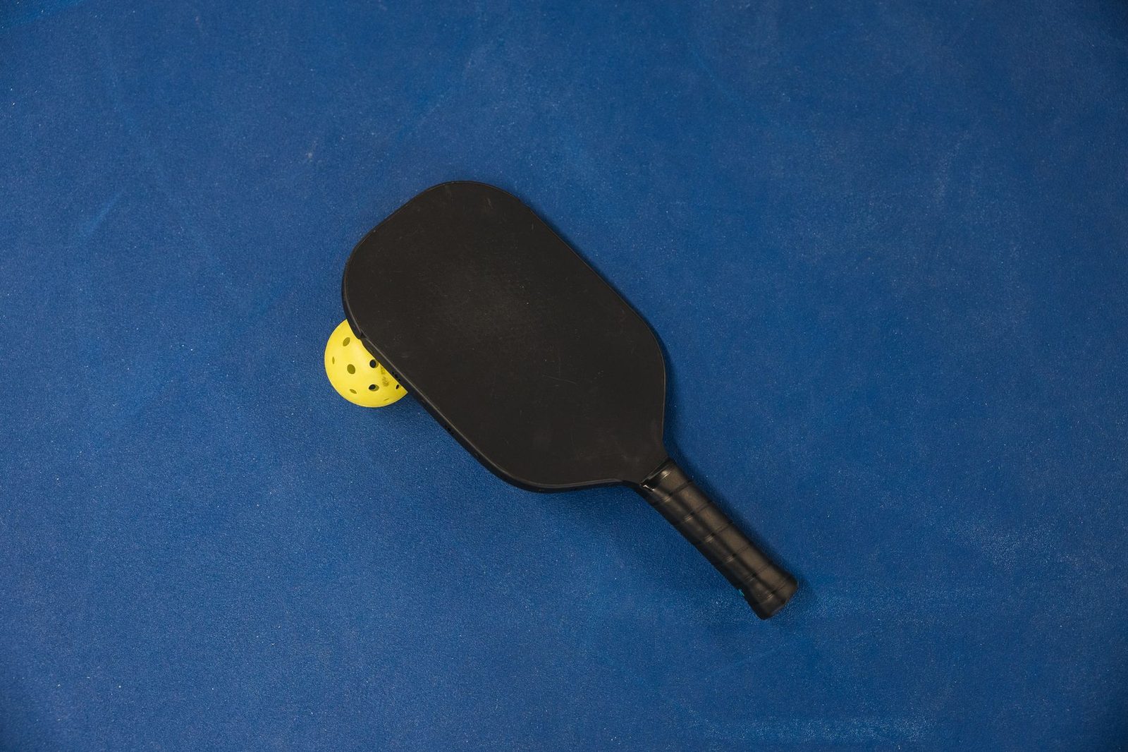 A pickleball paddle and perforated plastic ball on a blue surface