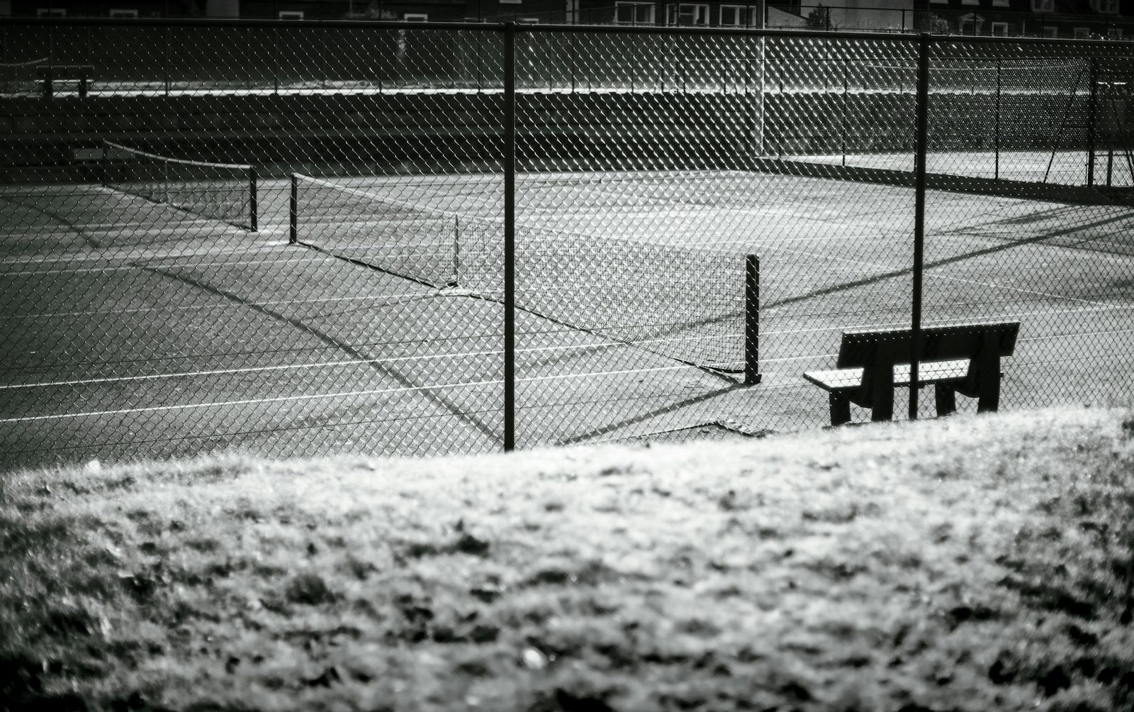 Empty tennis court with a bench and perimeter fence