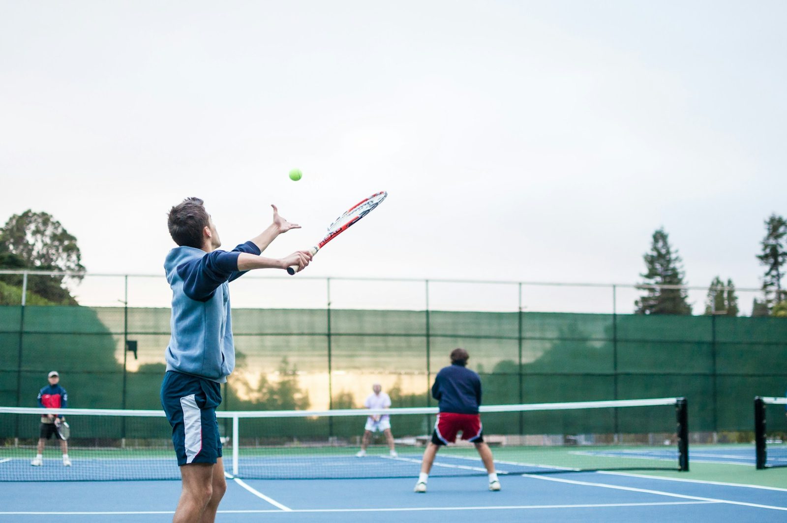 Four players in a doubles tennis match, with the net players positioned to intercept the return