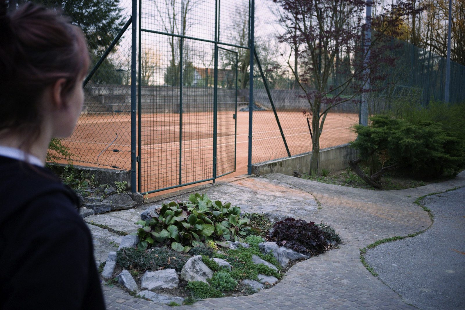 Adult watching a tennis court from the sideline in evening sunlight