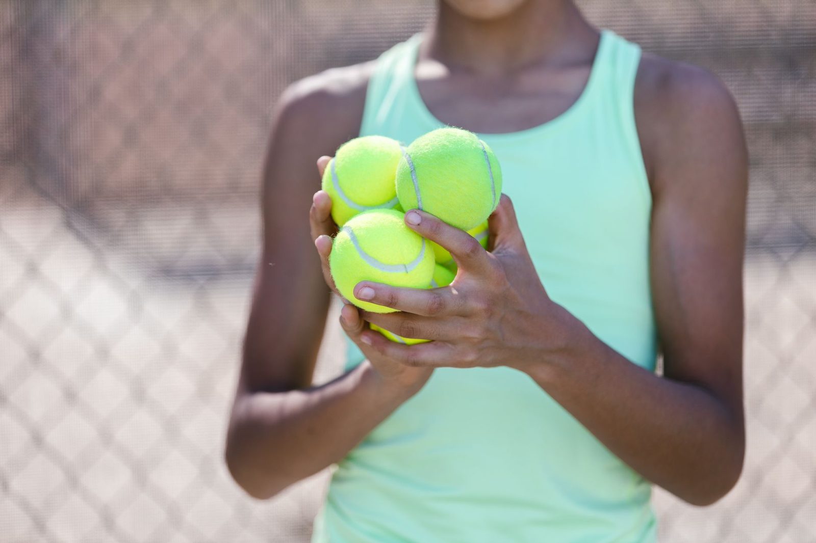 Close view of a person holding several tennis balls on a sunny day