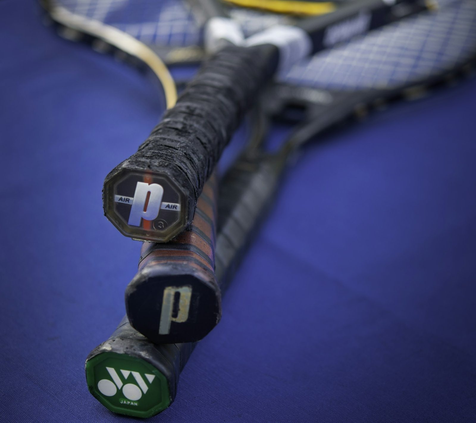 Close-up of a tennis racquet handle and grip on a blue surface