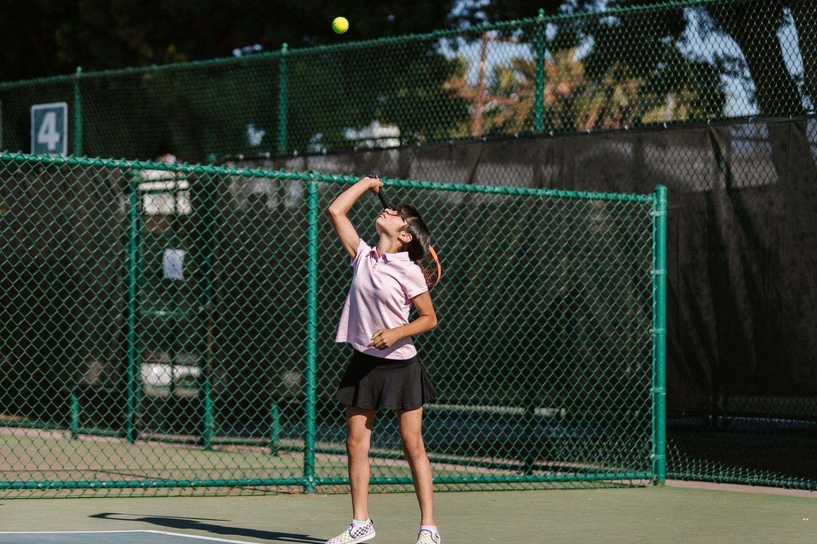 A young player practising her serve on a sunny outdoor court